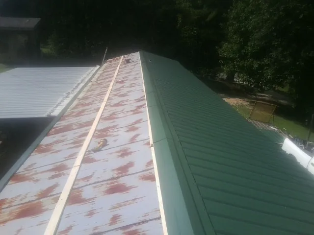 Old rusted panels beside newly installed green metal roofing — Wind Damage Roof Repair by Roofing Brothers in Purlear
