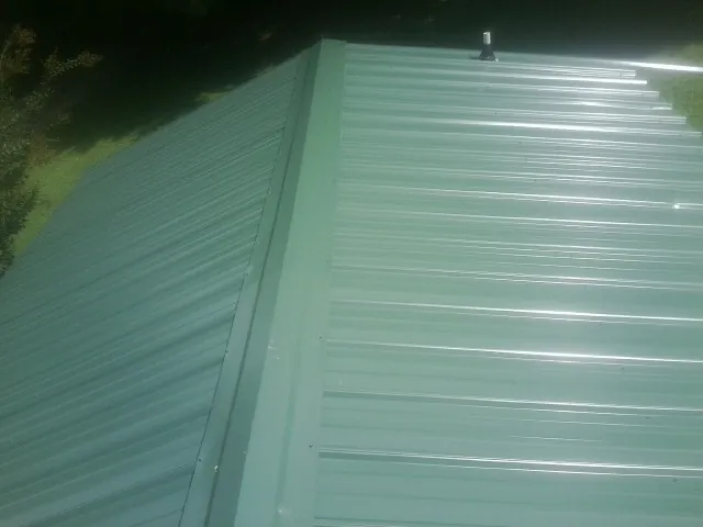 New green metal panels meeting at the ridge of a roof — Flat Roof Repair work by our crew in Purlear