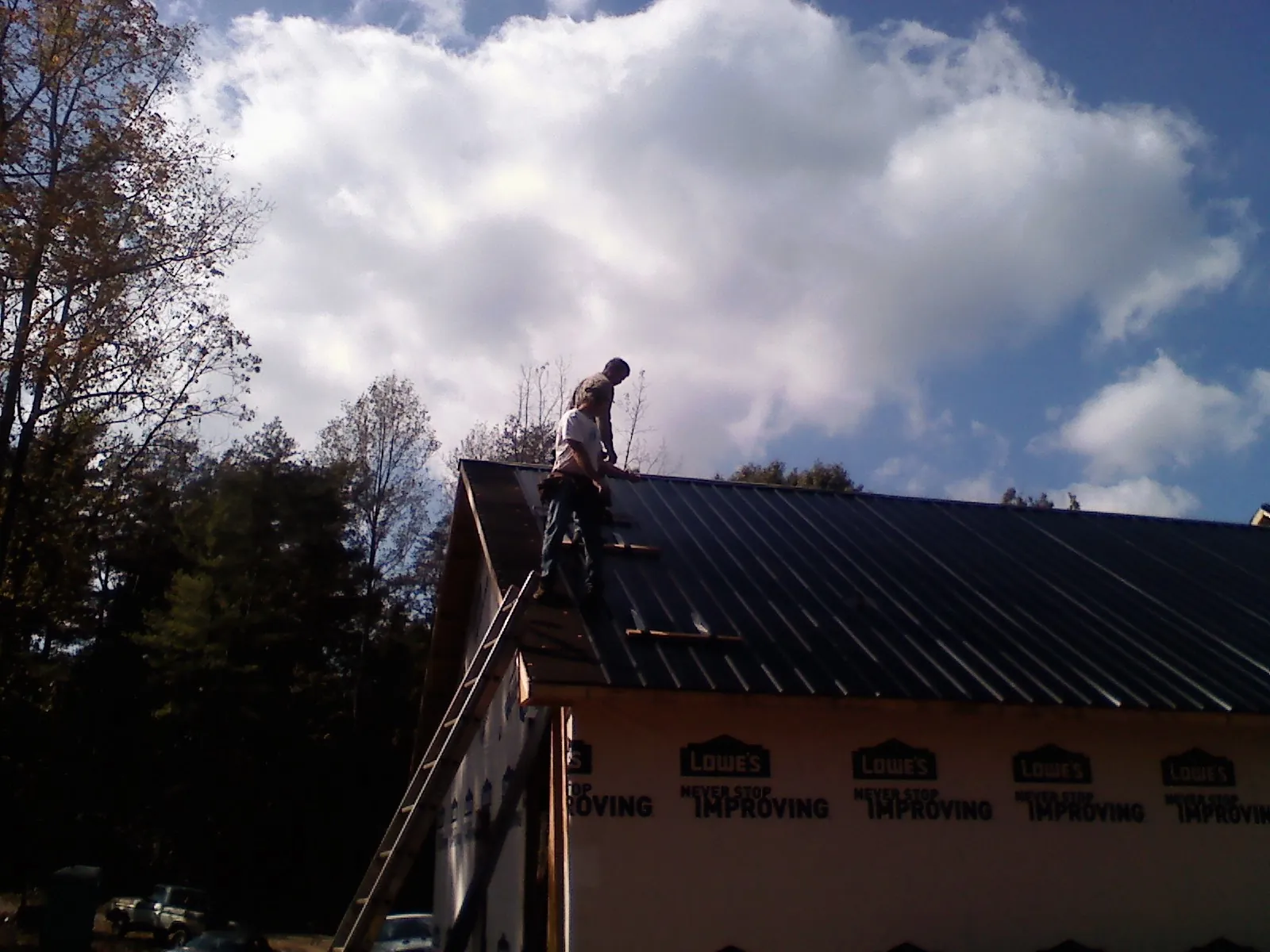 Roofer fastening dark metal panels high against a cloudy sky, from a Roof Inspection job in Purlear