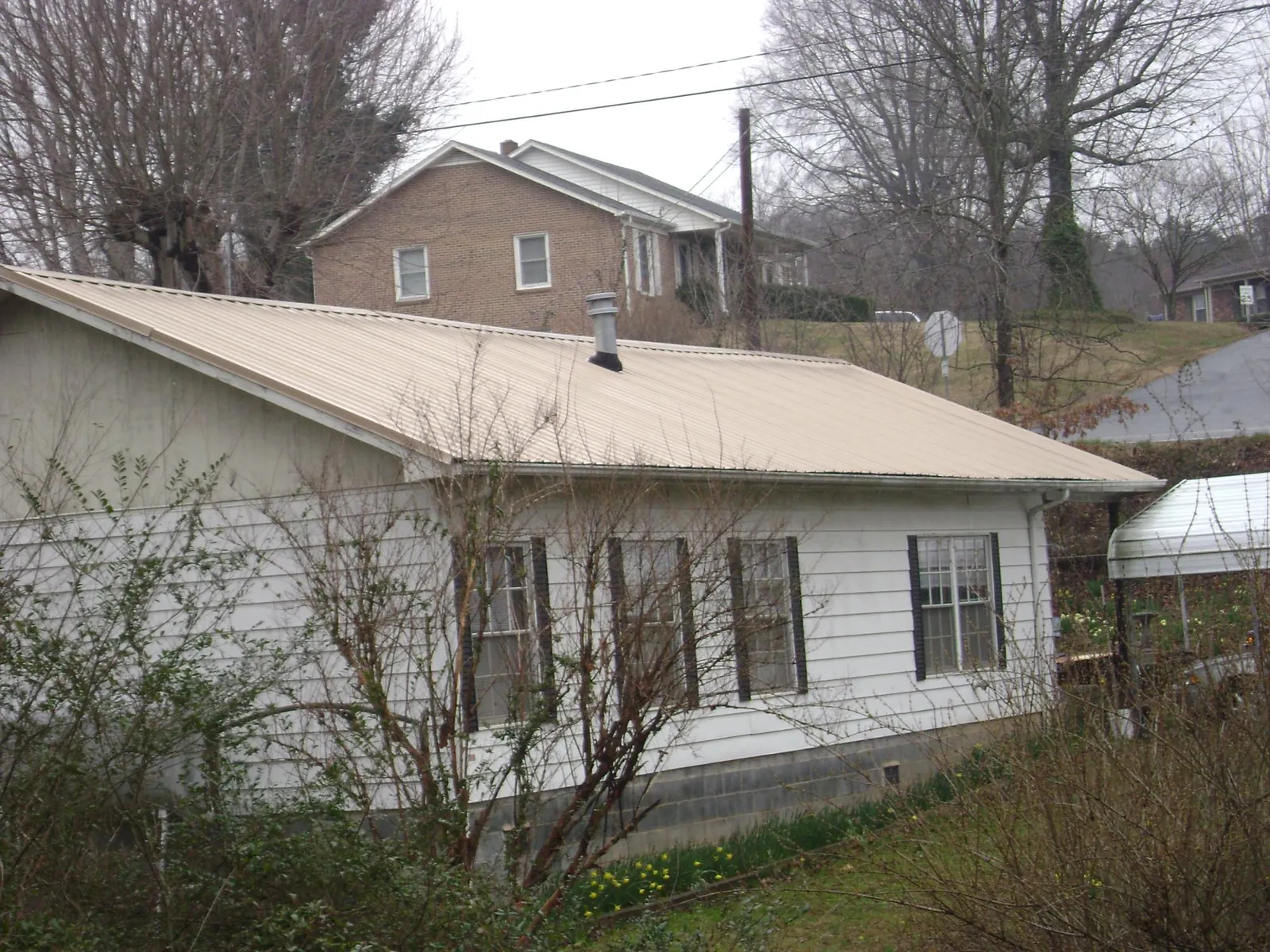 Tan metal roof on a white sided house set into a hillside — Commercial Roofing by Roofing Brothers in Purlear